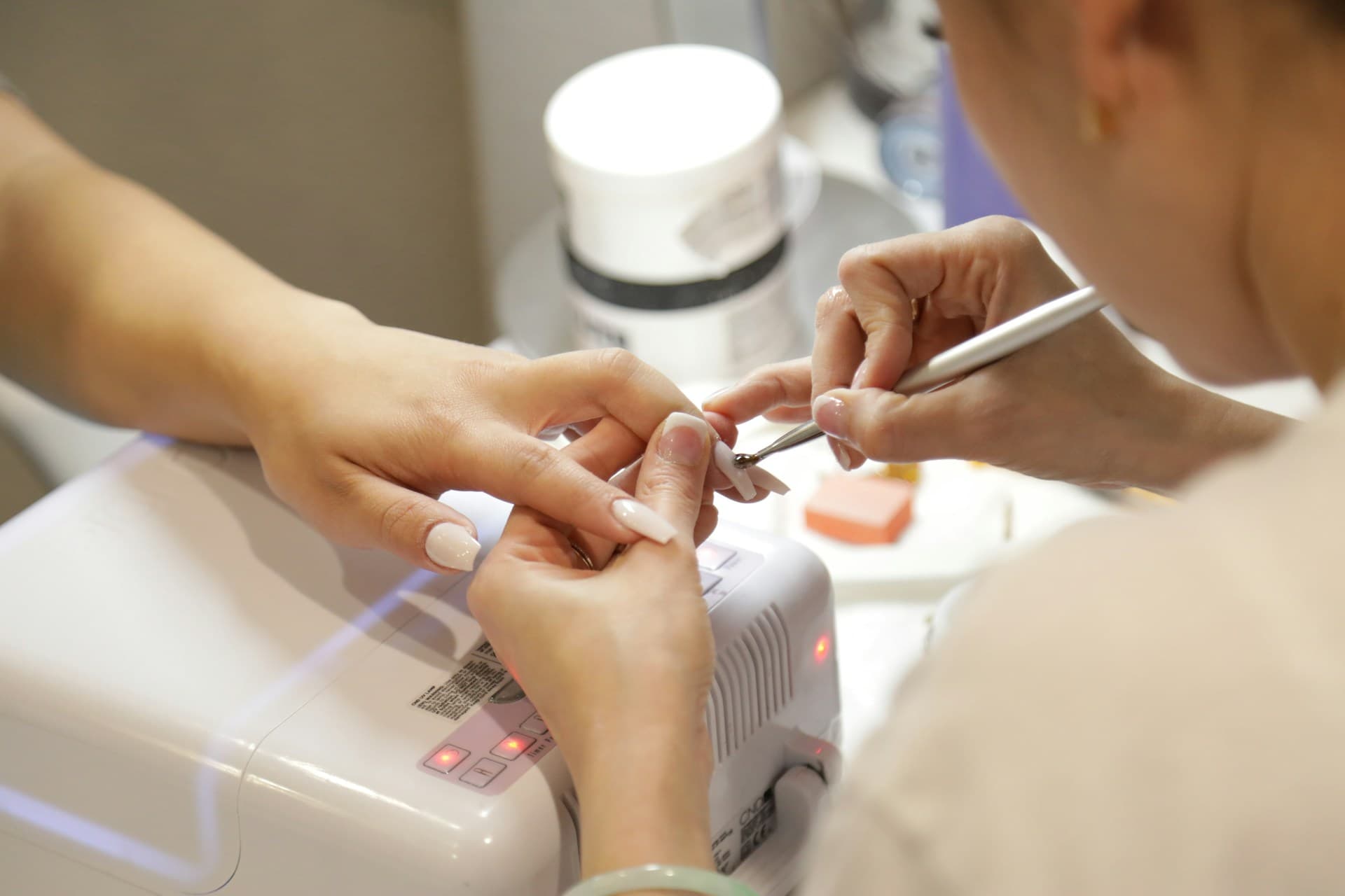 Manicurista trabajando sobre las uñas esculpidas de una clienta junto a una lámpara de secado
